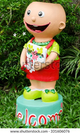 Smiling clay doll holding welcome signboard in garden