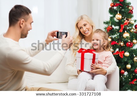 christmas, holidays, technology and people concept - happy family sitting on sofa and taking picture with smartphone at home