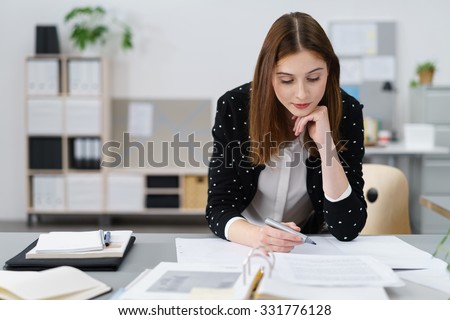 Attractive Young Office Woman Working on the Business Papers While Leaning on her Desk. Royalty-Free Stock Photo #331776128
