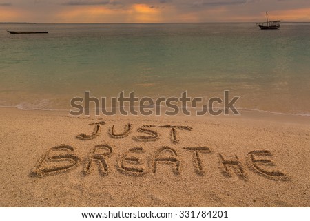 In the picture a beach at sunset with the words on the sand "Just breathe".