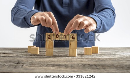 A person building a bridge of wooden cubes with the year 2016 written on them.