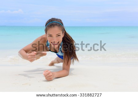 Core body workout - fitness woman planking doing forearm one arm spiderman knee to elbow crunch plank. Young Asian Chinese adult girl on beach strength training as part of a healthy lifestyle.