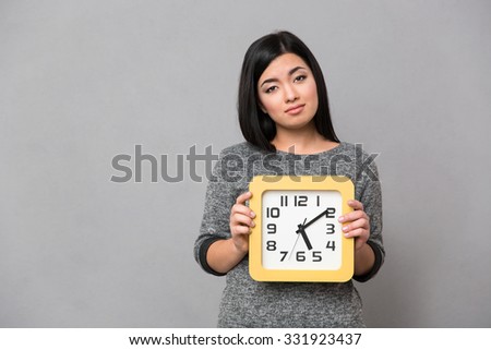 Portrait of a sad woman holding wall clock over gray background