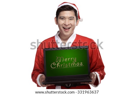 Handsome asian man wearing costume as santa claus and holding laptop with merry christmas writing