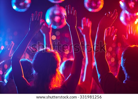Crowd of people with raised arms dancing in night club Royalty-Free Stock Photo #331981256