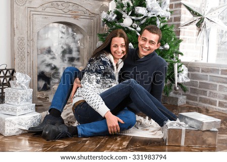 Happy young people give each other gifts by the fireplace near the Christmas tree.