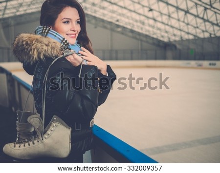 Cheerful girl with skates on ice skating rink 