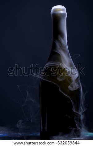 Closeup view of one new open full champagne wive sweet or dry drink green glass bottle with beautiful white smoke for celebration christmas or new year in studio on blue background, vertical picture
