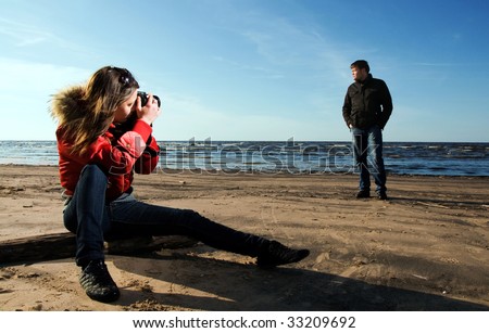 Young woman taking a photo of her boyfriend on the beach (Woman in focus)