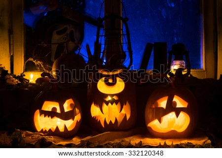 Photo composition from three pumpkins on Halloween. Embittered, the Cyclops and frightened pumpkins against an old window, dry leaves and a terrible ghost with a knife in a window