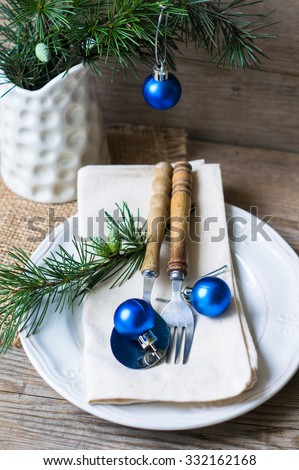 Christmas table setting with vintage silverware and pine tree branch in vase and blue christmas balls on the rustic background