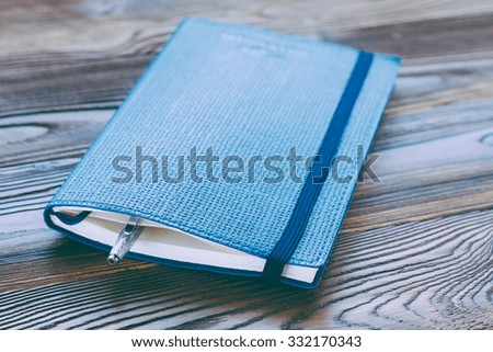 blue diary with a rubber band and silver ball pen on wooden background