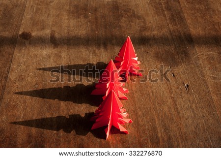 Christmas trees origami on rustic wood background with long shadows.