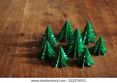 Christmas trees origami on rustic wood background with long shadows.