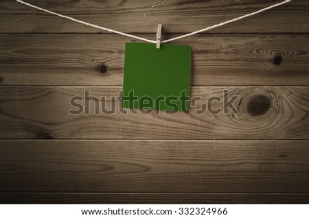 One individual square of festive dark green note paper, pegged to a string washing line with wood plank fence behind.  Low saturation and vignette gives a retro or vintage feel.