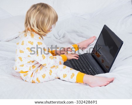 The baby is sitting in bed in my pajamas and barefoot with a laptop. Visible heel. A small child is working at the computer. The screen can be supplied of any advertising, screen saver or picture.