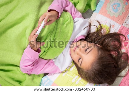 Little girl lying in bed with smartphone at home