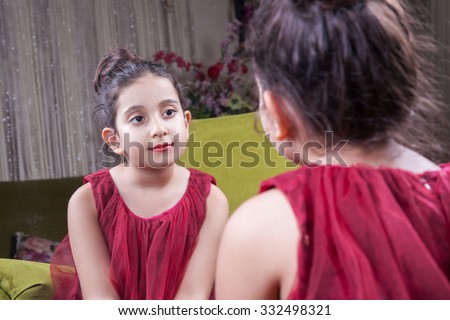 Small beautiful arab middle eastern girl with pretty red dress and lips posing and looking at herself in mirror. 8-10 years.
