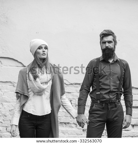 One beautiful stylish emotional couple of young woman and senior man with long beard standing close to each other outdoor in autumn street on brick wall background black and white, square picture