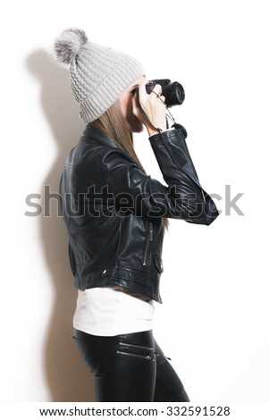 girl take photo with digital camera, wearing wool cap, leather jacket and black leggings, studio white, profile