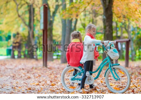 happy little girls riding a bike at beautiful autumn day outdoors