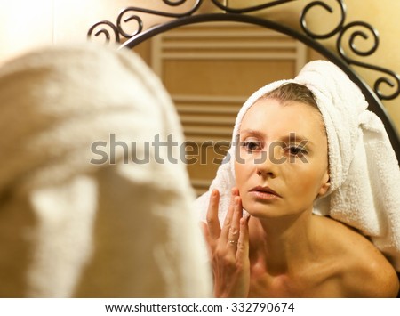 Middle-aged woman checking her face in bathroom mirror after shower