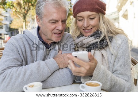Mature couple using a mobil phone at a bar terrace