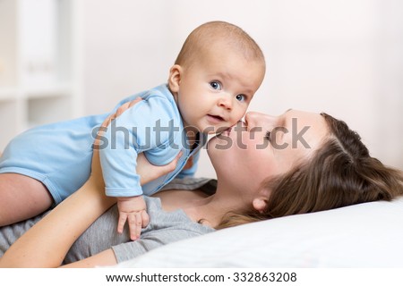Cute mother kissing baby lying on bed in nursery