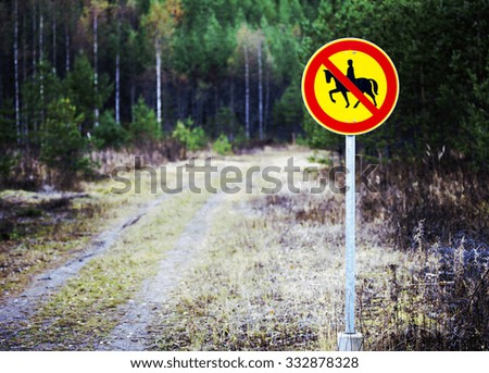 A warning sign telling that horseback riding is prohibited beyond this point. The sign has been composed to the right side to emphasize the composition for the road. Image has a vintage effect.