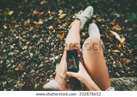 Teenage girl taking a selfie picture of her feet wearing white shoes on stony lakeside.