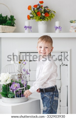Beautiful happy blond boy at the cage with a fireplace settle in the Studio