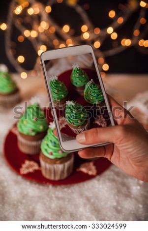 Close Up Of Human Hand Taking Picture Of Christmas Tree Cupcakes Using Smart Phone