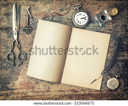 Open diary book and vintage writing tools on wooden table. Feather pen, inkwell, keys. Retro style toned picture with vignette
