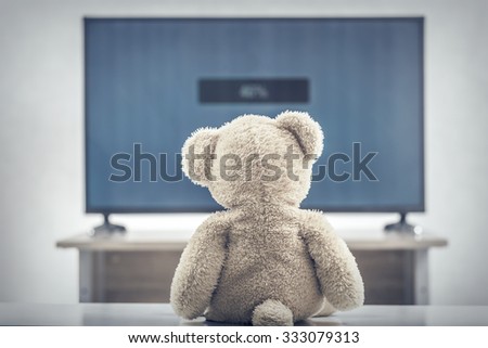 Teddy bear watching the television. Toned photo.