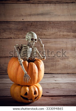 Skeleton is saluting on pumpkin and blur background.
