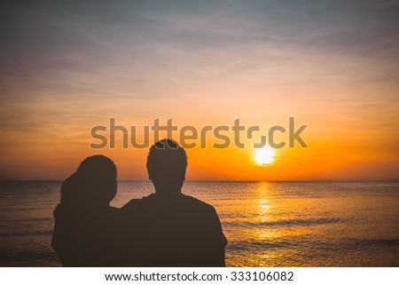 Young couple standing on the shore near the beach and watching the sunrise or sunset. Tropical landscape summer sea concept.