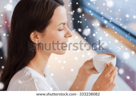 leisure, drinks, people and lifestyle concept - close up of smiling young woman drinking coffee at cafe with snow effect