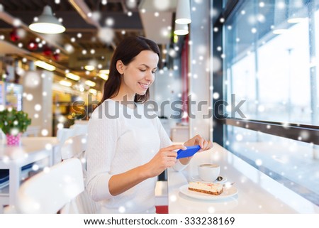 drinks, food, people, technology and lifestyle concept - smiling young woman taking picture with smartphone and drinking coffee at cafe with snow effect
