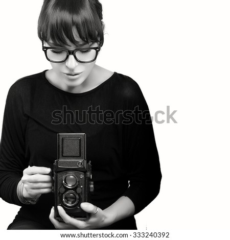 Attractive Young Woman Wearing Black Clothes and Glasses Capturing Photo Using Vintage Camera. Monochrome Portrait Isolated on White Background with Copy Space for Text