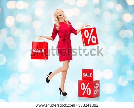 people, sale, discount and holidays concept - smiling woman in red dress with shopping bags over blue lights background