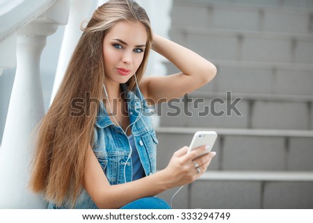 Young beautiful girl listening to MP3 player in the street. Funny teen girl singing and listening music from a smart phone with headphones. teen girl portrait outdoor witting on stairs