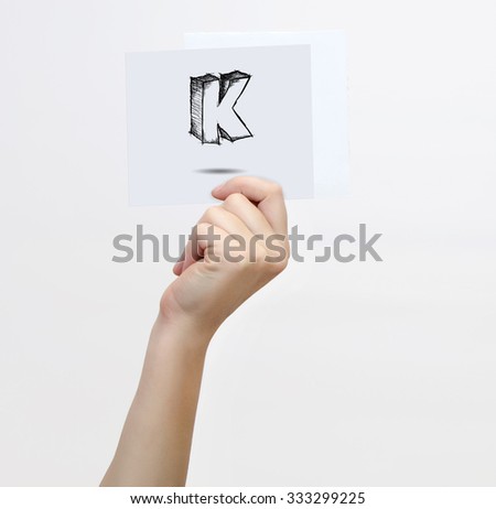 Hand holding a piece of paper with sketchy capital letter K, isolated on white.
