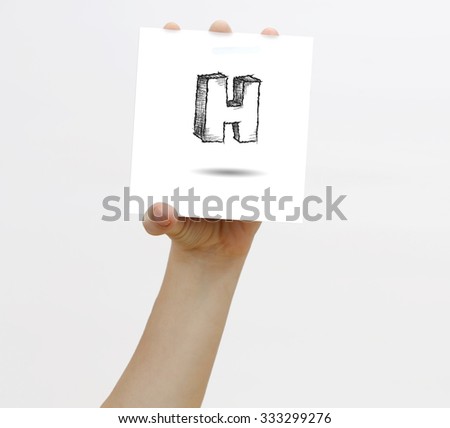 Hand holding a piece of paper with sketchy capital letter H, isolated on white.