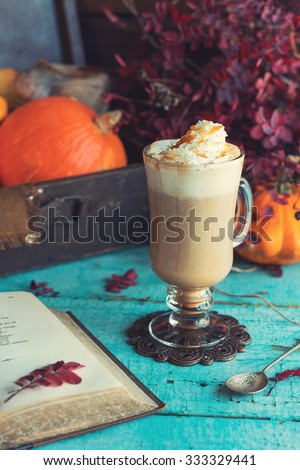Hot pumpkin spiced latte with whipped cream on top, on wooden background. Retro toning. Autumn still life vintage picture with book and ripe pumpkins in suitcase.