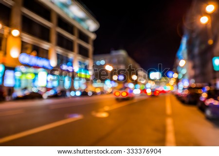 Nights lights of the big city, night avenue in the light of lanterns and illuminated shop windows. Wide-angle view, defocused image