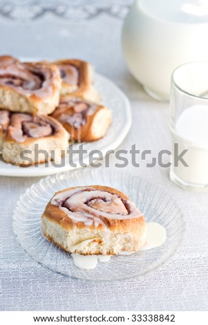 Sweet homemade cinnamon rolls served with a glass of milk. Focus is on bun in front. Shallow depth of field.