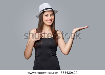 Happy woman in a hat  showing open hand palm with copy space for product or text , isolated on w gray background.