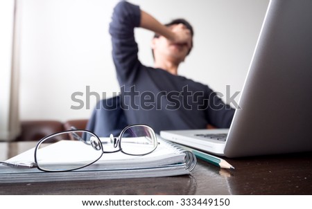 man with his hand holding his face taking a brake from working with laptop computer and notebook with eye glasses on wooden desk. concept of stress / rest / tension / failed / discourage / depression Royalty-Free Stock Photo #333449150