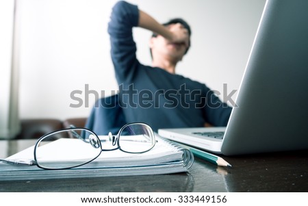 man with his hand holding his face taking a brake from working with laptop computer and notebook with eye glasses. concept of stress / rest / tension / failed / discourage / depressed. green filtered. Royalty-Free Stock Photo #333449156
