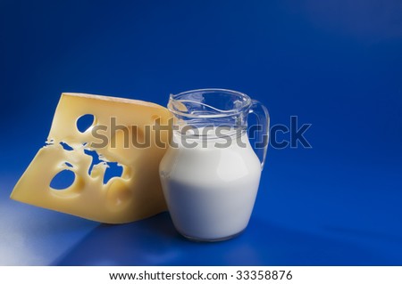 Hard cheese piece with milk jug on a blue background.